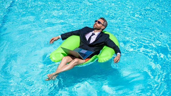 stock image man trader work and relax in swimming pool on ring. man trader work and relax with laptop. photo of man trader work and relax in pool. man trader work and relax.