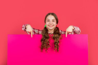 Reklam için fotokopi alanı olan boş pembe kağıdın arkasında mutlu bir çocuk. işaret parmağı.
