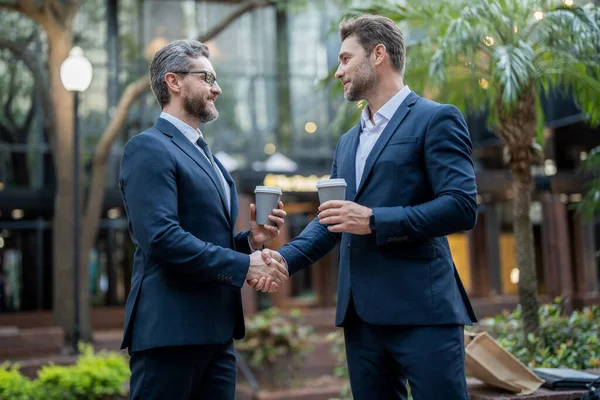photo of two business partners dealing negotiation. two business partners dealing negotiation. two business partners dealing negotiation outdoor. two business partners holding coffee dealing