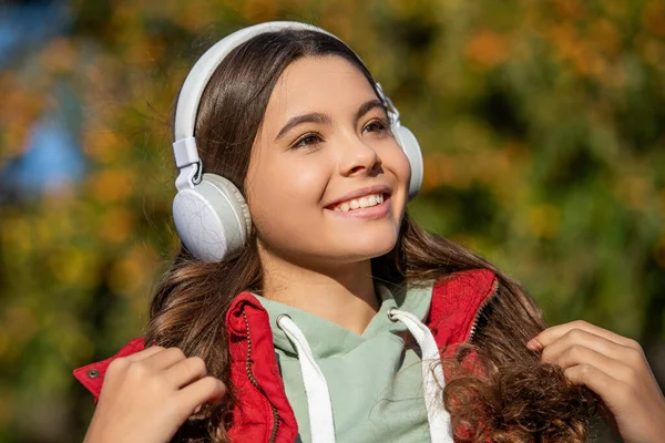 stock image smiling teen girl listening music outside. teen girl listening music wearing headphones. photo of teen girl listening music. teen girl listening music outdoor.