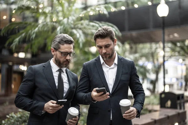 Dışarıda telefonu olan iş arkadaşları. Takım elbiseli iş arkadaşları. İş arkadaşlarının telefon ve kahveli fotoğrafları. Sokakta telefonu olan iş arkadaşları.