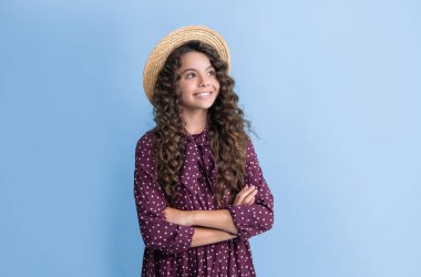 Hasır şapkalı mutlu çocuk, mavi arka planda uzun kahverengi kıvırcık saçlı..