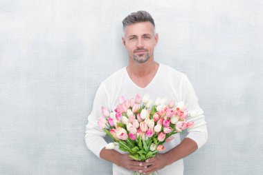 mature man with spring tulips isolated on blue background. photo of man with spring tulips. man with spring tulips. man with spring tulips in studio.
