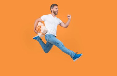 Energetic courier man running with gift box in midair yellow studio background. Fast courier delivery. Courier service.