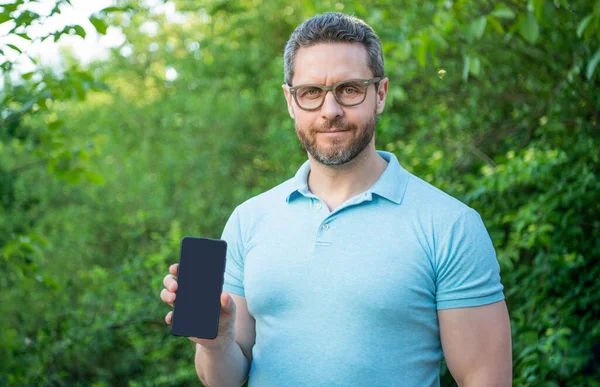 スマートフォンを屋外で見せる陽気な男 スマホの画面をコピースペースで提示する男 スマートフォンを見せる男の写真です スマートフォンを — ストック写真