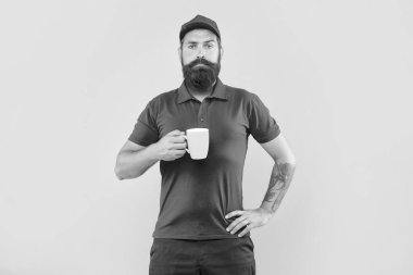 Serious bearded guy in casual red cap and tshirt holding mug yellow background, coffee.