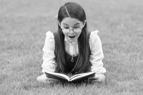一个令人惊讶的女孩躺在草地上看书的画像 在户外读书的少女 — 图库照片