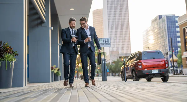 happy businessmen walk with phone outdoor. businessmen walk with phone in suit. photo of businessmen walk with phone. businessmen walk with phone in the street.