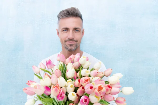 cheerful man with valentines day bouquet isolated on blue background. photo of man with valentines day bouquet for holiday. man with valentines day bouquet. man with valentines day bouquet in studio.
