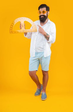 Adam arka planda geometri açısını tutuyor, işaret parmağı. İnsan tutuşu geometri iletkeninin fotoğrafı. Geometri açıölçer sarı renkte izole edildi. Stüdyoda geometri açıölçer var..