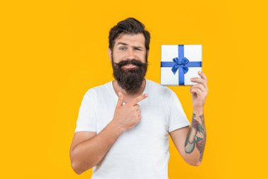 Sakallı adam hediye kutusunu stüdyoda, işaret parmağıyla tutuyor. Sakallı adam hediye kutusunu arka planda tutuyor. Sakallı adamın hediye kutusundaki fotoğrafı. Sakallı adam, hediye kutusunu sarıda sakla..