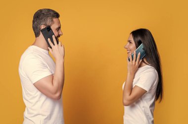 Cep telefonuyla konuşan gülümseyen bir çift birbirlerine bakıyor. Mutlu adam ve kız cep telefonu arama stüdyosu yapıyorlar. Cep telefonu sohbeti. Mobil iletişim.