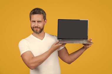 cheerful man showing app on screen with copy space. man showing app isolated on yellow background. man showing laptop app in studio. man showing app on laptop.