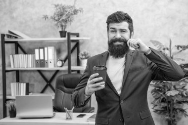 Gülümseyen sakallı iş adamı ofiste fotokopi yeri ve sabah kahvesi ile paket kahve içiyor..