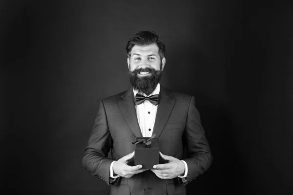glad man in tuxedo bow tie formalwear on black background with gift box. boxing day.
