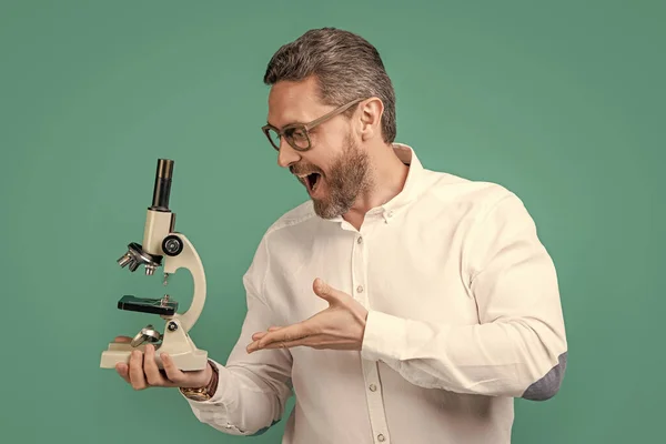 amazed man microscope for invention. photo of man holding microscope, invention. man with invention microscope isolated on blue background. man hold invention microscope in studio.