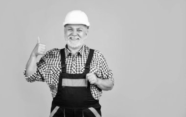 Sarı arka planda miğferli, yaşlı, neşeli bir inşaatçı..