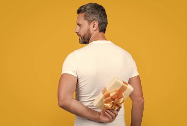 man hiding present box for holiday. photo of man holding occasion present box. man hold present box isolated on yellow background. man hold present box in studio.