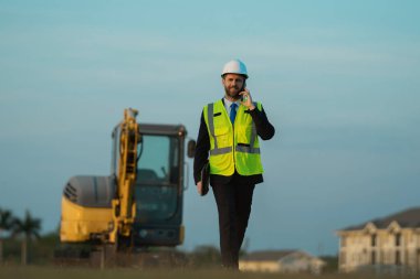 Mimar işgali adamı dışarıda telefonla konuşuyor. Mimar işgali mühendisi kask takıyor. Mimarlık mesleğinin fotoğrafı. Mimar işgali adamı..