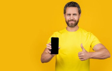 Stüdyoda akıllı telefon uygulaması gösteren bir adam, kopyalama alanı. Akıllı telefon uygulaması gösteren bir adamın fotoğrafı. Akıllı telefon uygulaması gösteren adam sarıda izole edildi. Adam arka planda akıllı telefon uygulaması gösteriyor.