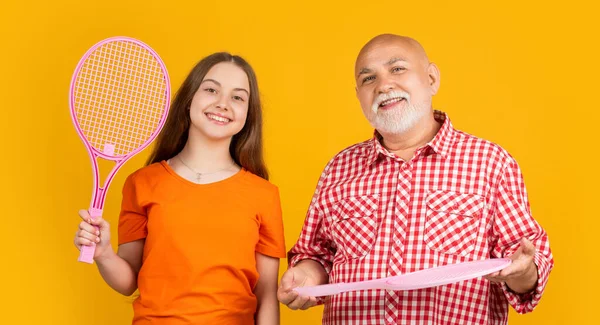 stock image happy teen child with grandfather with badminton racket on yellow background.