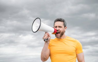 man in yellow shirt speak in megaphone on sky background.