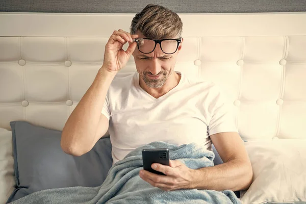 躺在床上打着眼镜在电话里聊天的成熟男人 — 图库照片