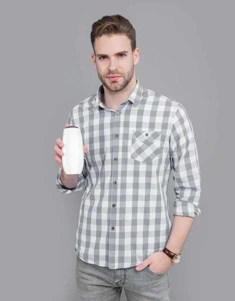 stock image young guy hold bottle of aftershave product. guy hold aftershave product isolated on grey background. guy with aftershave product in studio. aftershave product for guy.