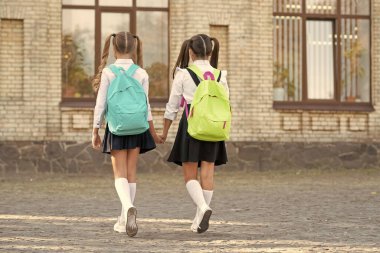 back view of two sisters with school backpack walking together outdoor.