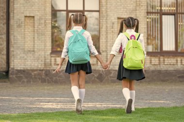 back view of two schoolgirls with school backpack walking together outdoor. childhood.