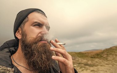 caucasian bearded man smoking cigarette. photo of man smoking cigarette in the mountain. man smoking cigarette outdoor. man with beard smoking cigarette.