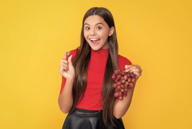 surprised teen child hold bunch of grapes on yellow background.