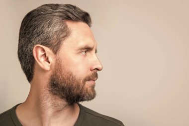 Gri arka planda sakallı beyaz bir adamın portresi var. Stüdyoda sakallı beyaz bir adam. Sakallı beyaz bir adamın fotoğrafı. Kirli sakallı beyaz adam tişört giyiyor..