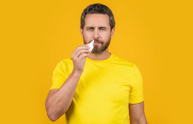 Adam stüdyoda burun tıbbı kullanıyor. Burun tıbbı damlaları olan bir adamın fotoğrafı. Burun tıbbı olan adam sarıda izole edilmiş. Geçmişinde burun tıbbı olan bir adam..