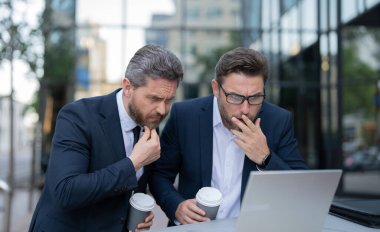 Kafası karışmış tüccar işadamları online olarak dizüstü bilgisayarla serbest çalışıyorlar. Tüccarların internetten serbest iş yaparken çekilmiş bir fotoğrafı. İki tüccar online olarak serbest çalışıyor. İşlemciler online olarak açık havada serbest çalışıyorlar..