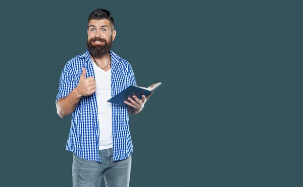幸せな髭の男は灰色の背景で本を読んでいる 親指を上げて — ストック写真