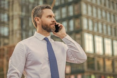 handsome businessman having smartphone call in the street. businessman call on smartphone outside. photo of businessman call on smartphone and talk. businessman has smartphone call outdoor.