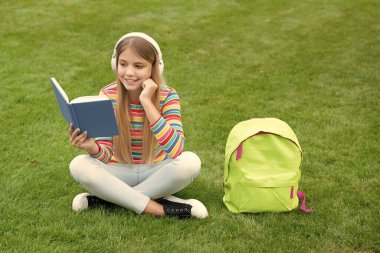 Mutlu genç kız kitap okuyor kulaklık dinliyor okuldan sonra çimlerin üzerinde oturuyor, ödev yapıyor..