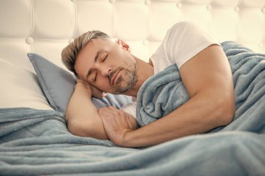 Olgun bir adam yatakta dinleniyor. Sabah erken saatlerde.