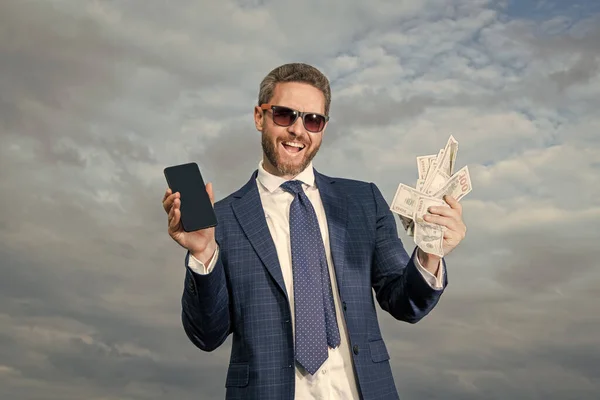 cheerful betting man with lottery money outdoor. betting man with lottery money hold phone. photo of betting man with lottery money. betting man with lottery money on sky background.