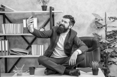 Mutlu patron akıllı telefona gülümsüyor ofis masasında bağdaş kurup oturuyor, selfie çekiyor..