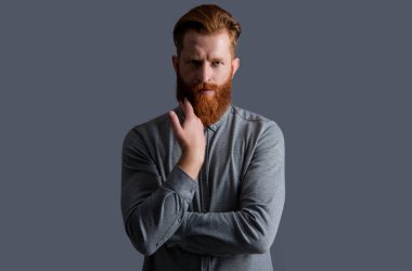 Yakışıklı, tıraşsız adamın yüzünde sakal ve bıyık var. Gri arka planda sakallı ve bıyıklı traşsız bir adam. Traşsız adamın stüdyo çekimi. Bıyık ve sakal bakımı.