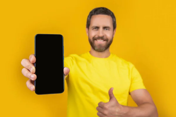 stock image man showing smartphone app isolated on yellow, selective focus. man showing smartphone app on background. man showing smartphone app in studio. photo of man showing smartphone app.