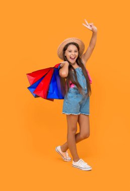 happy teen girl with shopping bags show peace on yellow background. full length.