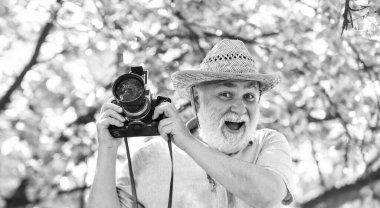 Yaşlı sakallı adam pembe çiçeklerin fotoğrafını çekiyor. Profesyonel fotoğrafçı tasarımcısı. Mutlu emeklilik. Turist adam kiraz çiçeğinin kamerasını kullanır. Çiçek açan fotoğrafçılıkta sakura. bahar çiçekleri.
