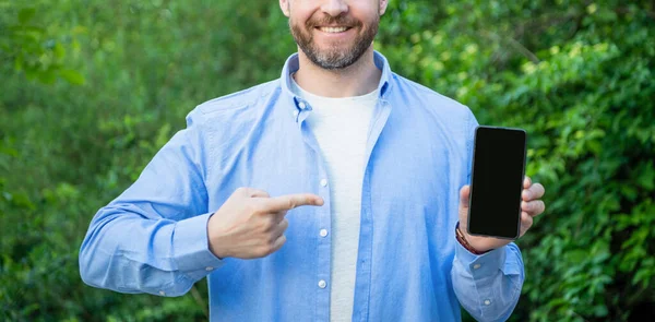コピースペース付きのスマートフォンの画面で指を提示し指差す男 スマートフォンを スマートフォンを提示する男 スマートフォンの屋外で — ストック写真