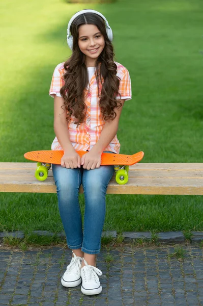 ヘッドフォンでスケートボードを持つ陽気な10代の女の子 スケートボードを持ってる10代の女の子 スケートボードを持つ10代の女の子は音楽を聴く スケートボードのアウトドアを持つ10代の女の子 — ストック写真
