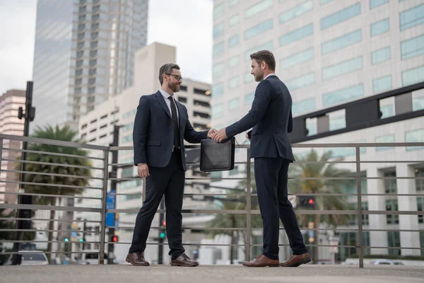 full length of two smiling business partners dealing outdoor. photo of two business partners dealing. two business partners dealing. two business partners dealing with handshake.
