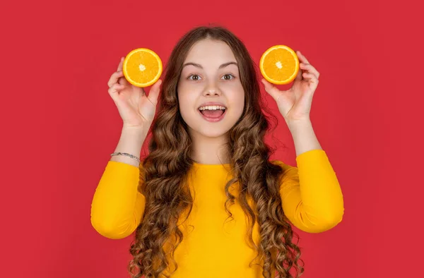 stock image amazed teen kid hold orange fruit on redbackground. juicy orange girls