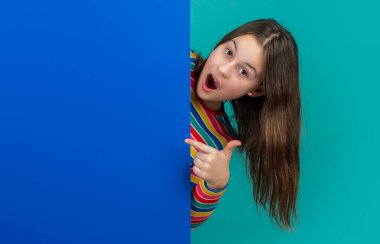 Reklam için fotokopi alanı olan boş mavi kağıdın arkasında büyülenmiş bir çocuk. işaret parmağı.